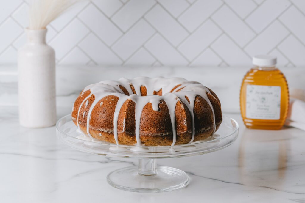 Bundt cake with cream cheese icing and jar of honey in the background